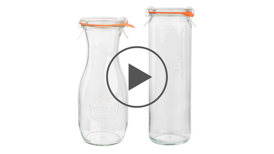 Стеклянная бутылка и цилиндрическая банка Weck с оранжевыми уплотнительными резинками и металлическими зажимами, с логотипом Weck на белом изолированном фоне.