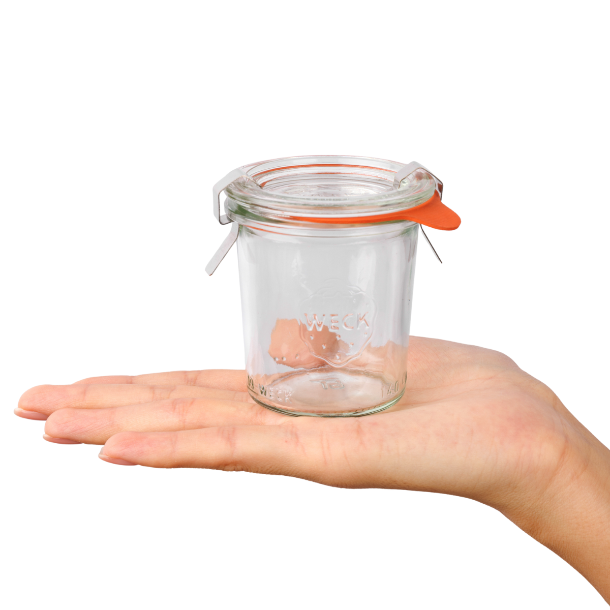 Ладонь аккуратно держит мини-стеклянную баночку Weck с гравированным логотипом и оранжевым уплотнительным кольцом, идеально подходящую для сервировки десертов или хранения специй.