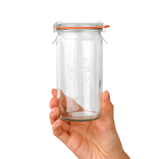Рука держит прозрачную стеклянную банку WECK с оранжевой резинкой и зажимами, четкая гравировка логотипа WECK, на белом фоне, стенки плотные.