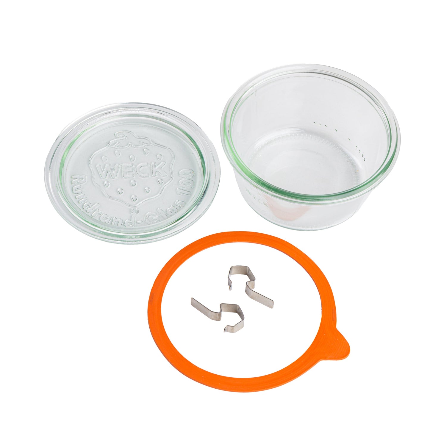 Разобранные элементы круглой стеклянной банки Weck: прозрачная крышка с гравировкой логотипа Weck, оранжевый силиконовый уплотнитель и металлические зажимы, на белом фоне.