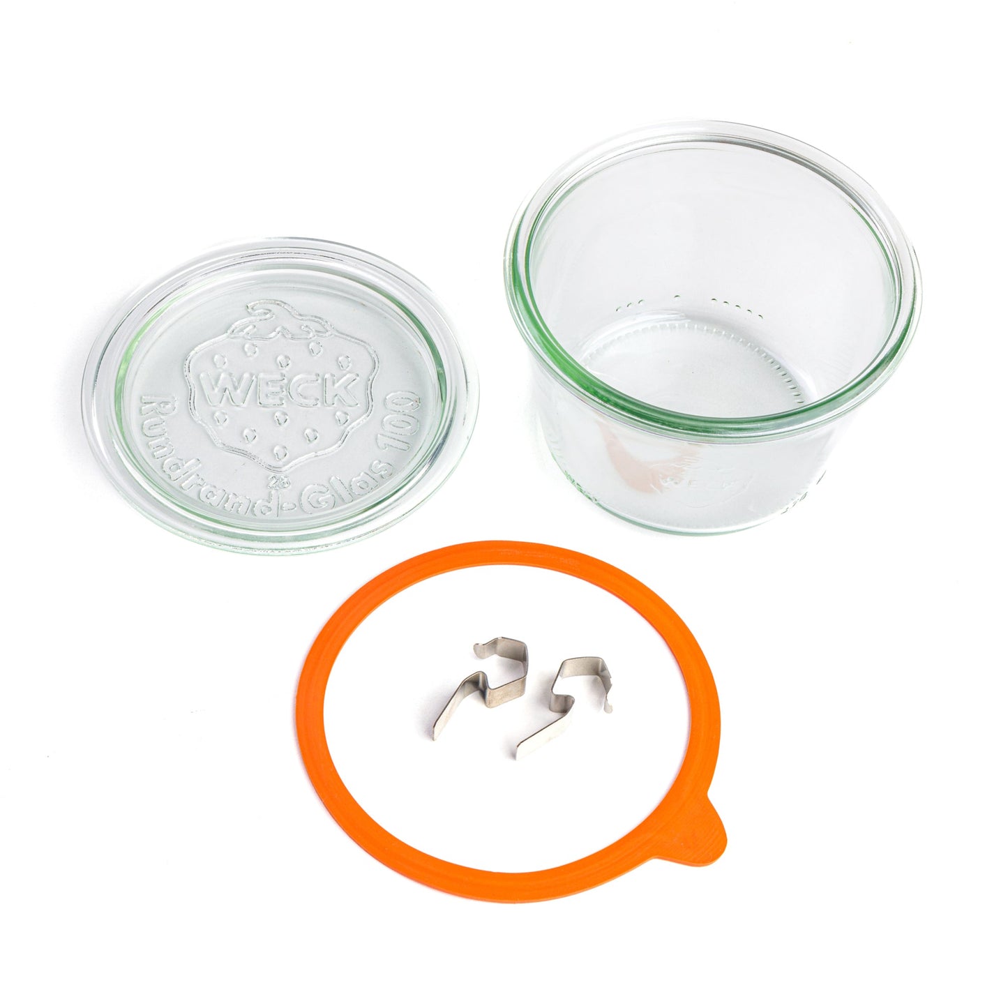 Разобранные элементы круглой стеклянной банки Weck: прозрачная крышка с гравировкой логотипа Weck, оранжевый силиконовый уплотнитель и металлические зажимы, представленные отдельно на белом фоне.