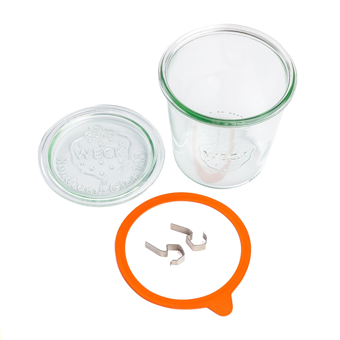 Отдельные компоненты круглой стеклянной банки Weck: прозрачная крышка с гравировкой логотипа Weck, оранжевый силиконовый уплотнитель и металлические зажимы, на белом фоне.