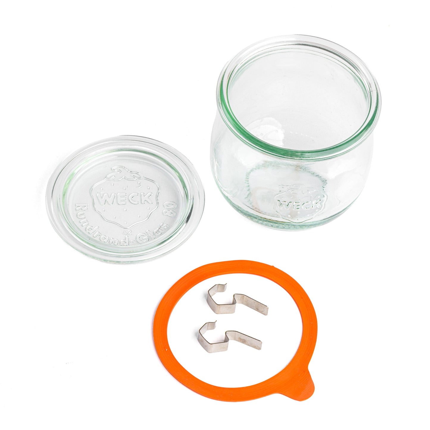 Стеклянная банка WECK овальной формы, разобранная на части: отдельная крышка с выдавленным логотипом WECK и 'Rundrand-Glas 100', оранжевая уплотнительная резинка и металлические зажимы, композиция на белом фоне.