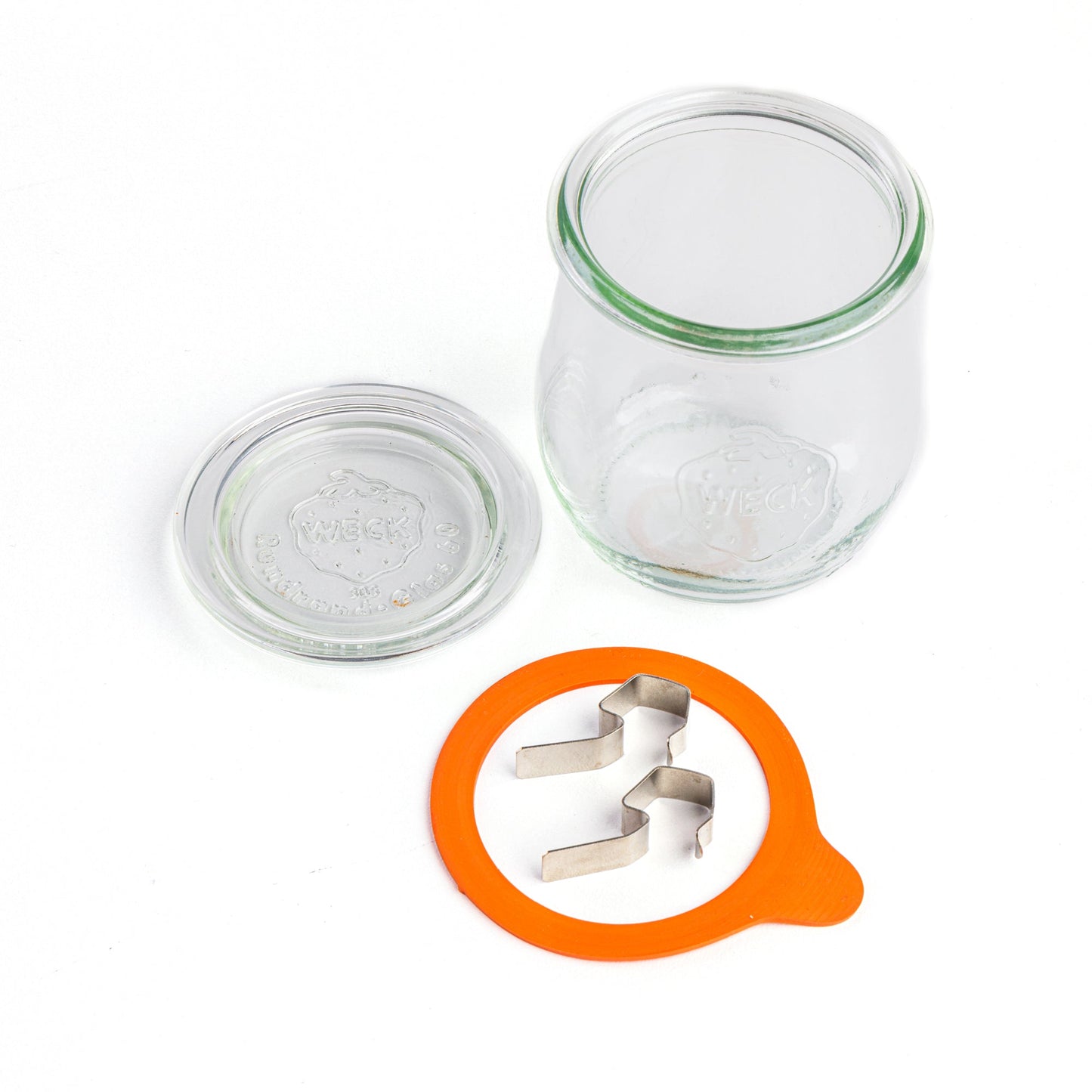 Компоненты стеклянной банки WECK тюльпанообразной формы, разложенные на части, вид сверху. Отдельная крышка с гравировкой логотипа WECK, оранжевая уплотнительная резинка и металлические зажимы, белый фон.