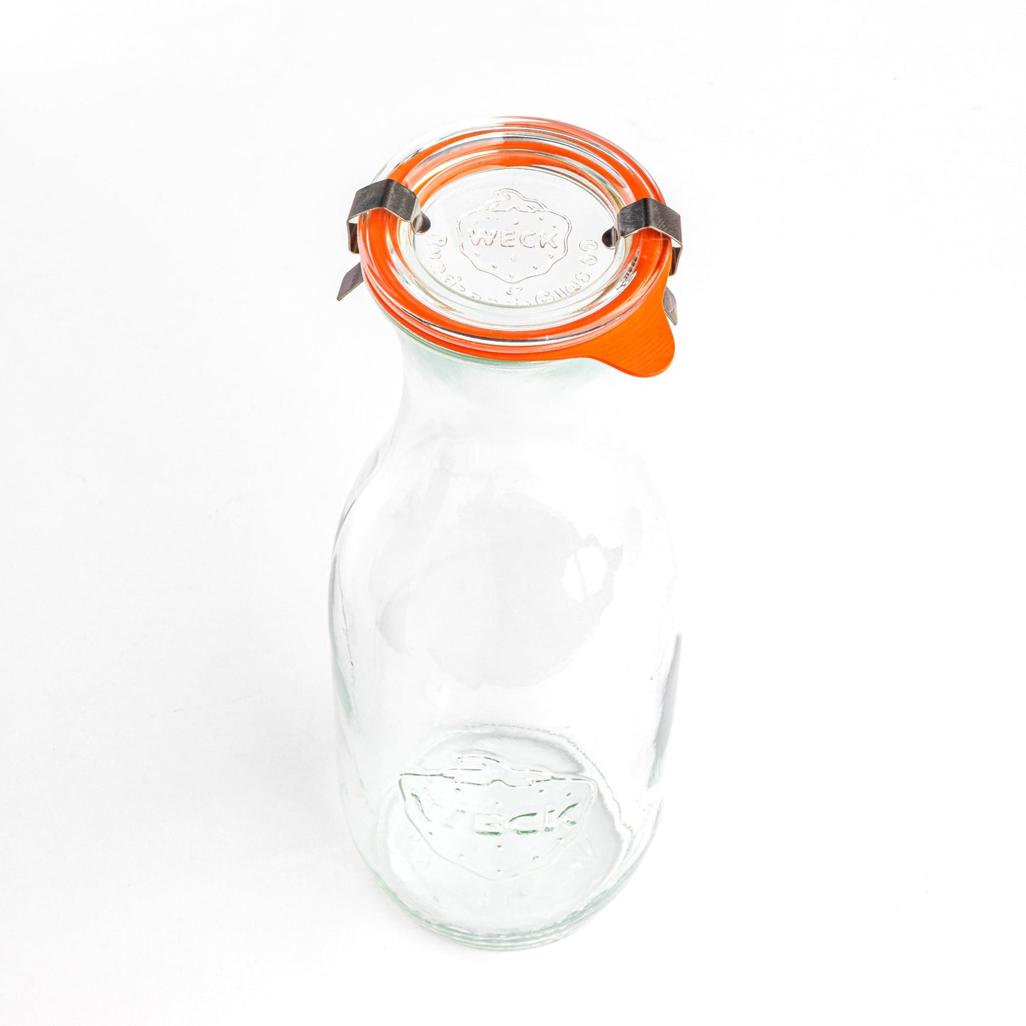 Вид сверху на стеклянную банку WECK с узким горлом и расширяющимся основанием, закрытую оранжевой уплотнительной резинкой и стальными зажимами. Гравировка логотипа WECK и надпись 'Rundrand-Glas 100' четко видны на крышке, белый фон.