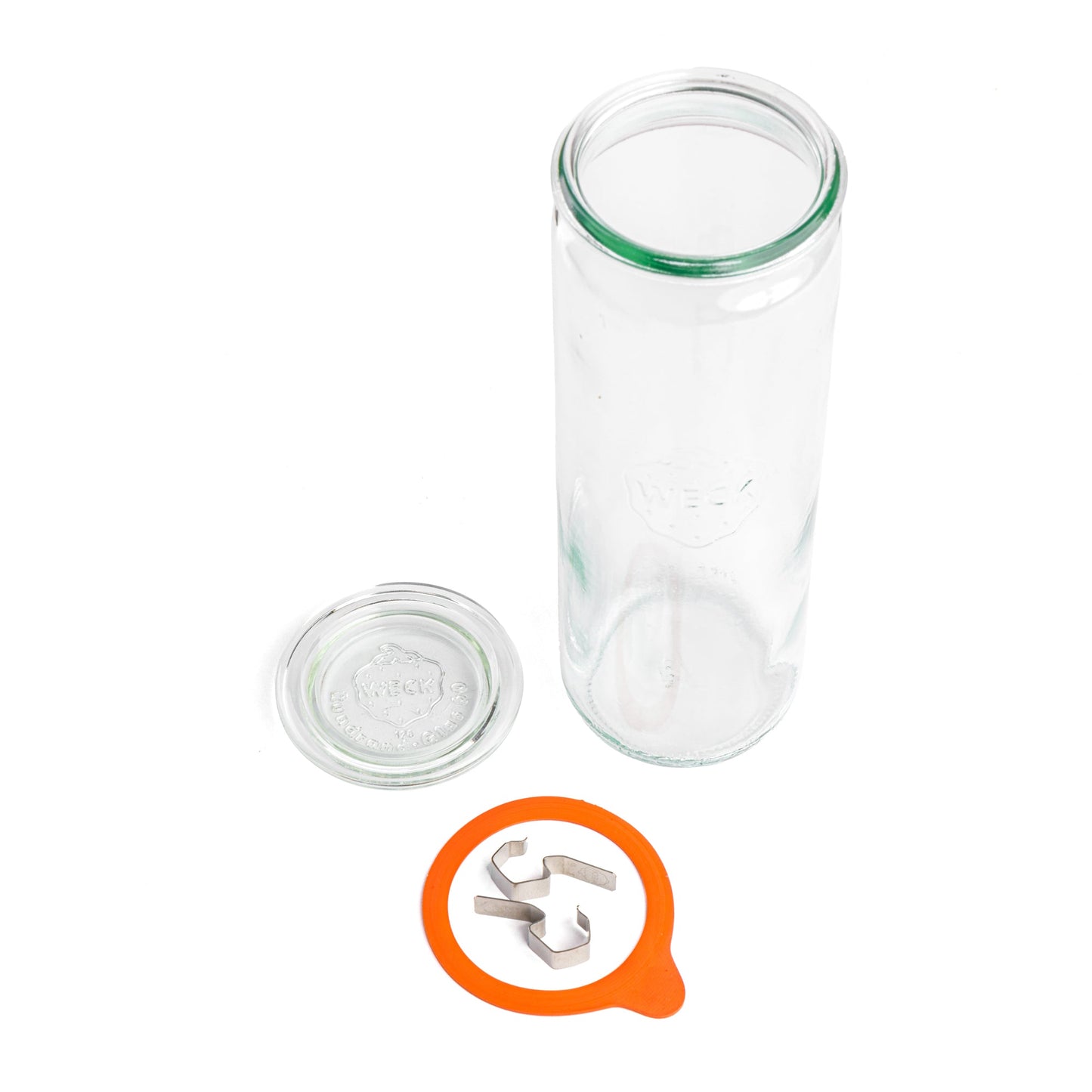 Разобранная цилиндрическая стеклянная банка Weck с толстыми стенками на белом фоне, показывающая отдельно лежащую крышку, стеклянную банку и металлические зажимы.