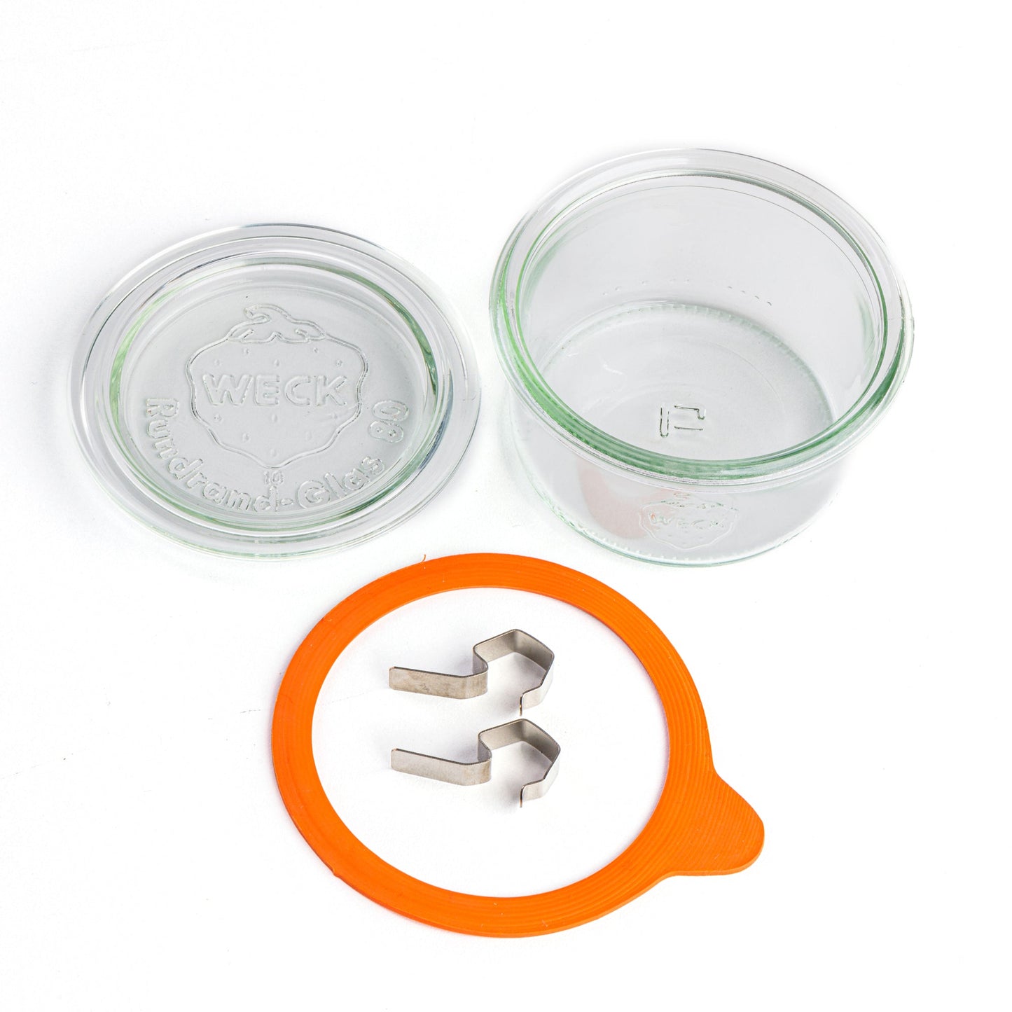 Компоненты стеклянной банки Weck: прозрачная крышка с эмбоссированным логотипом, оранжевый силиконовый уплотнитель и металлические зажимы, представленные отдельно на белом фоне.